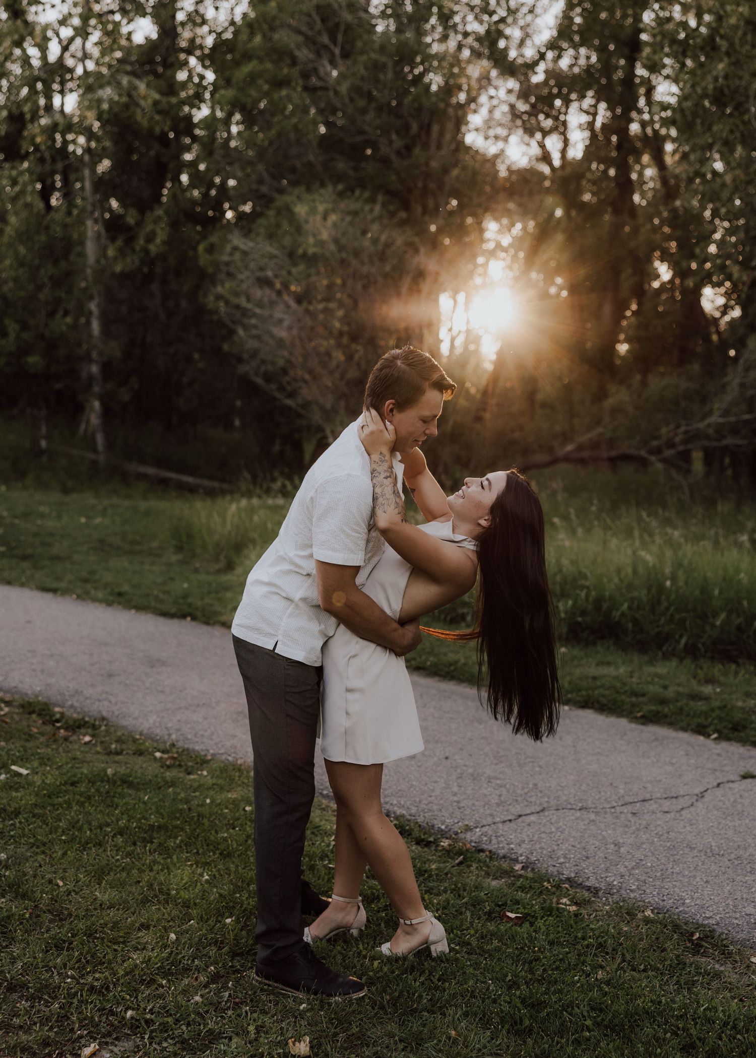 Romantic sunset embrace on a path with golden light filtering through trees.