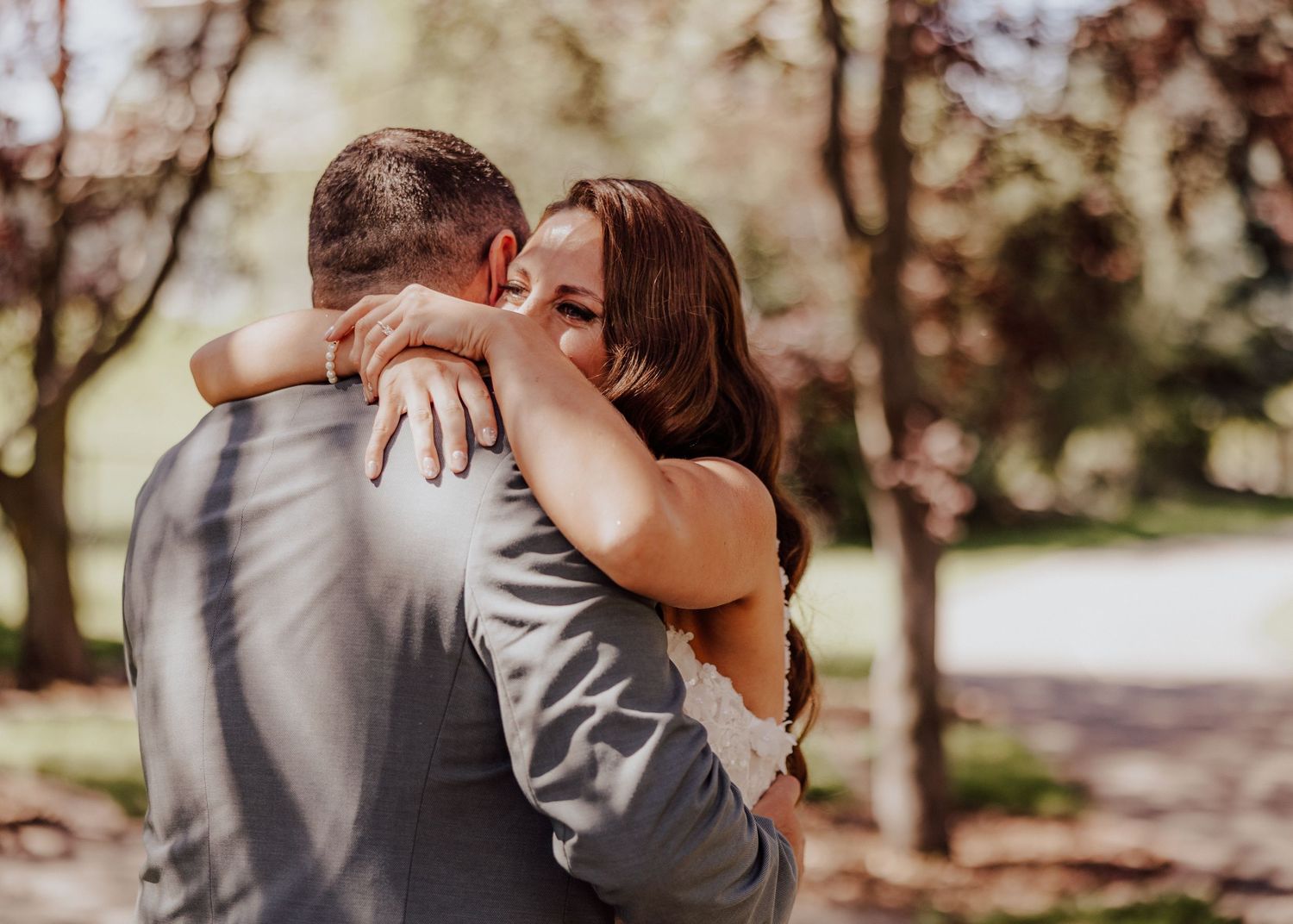 A romantic embrace between a couple outdoors during golden hour with sunlit trees in the background.
