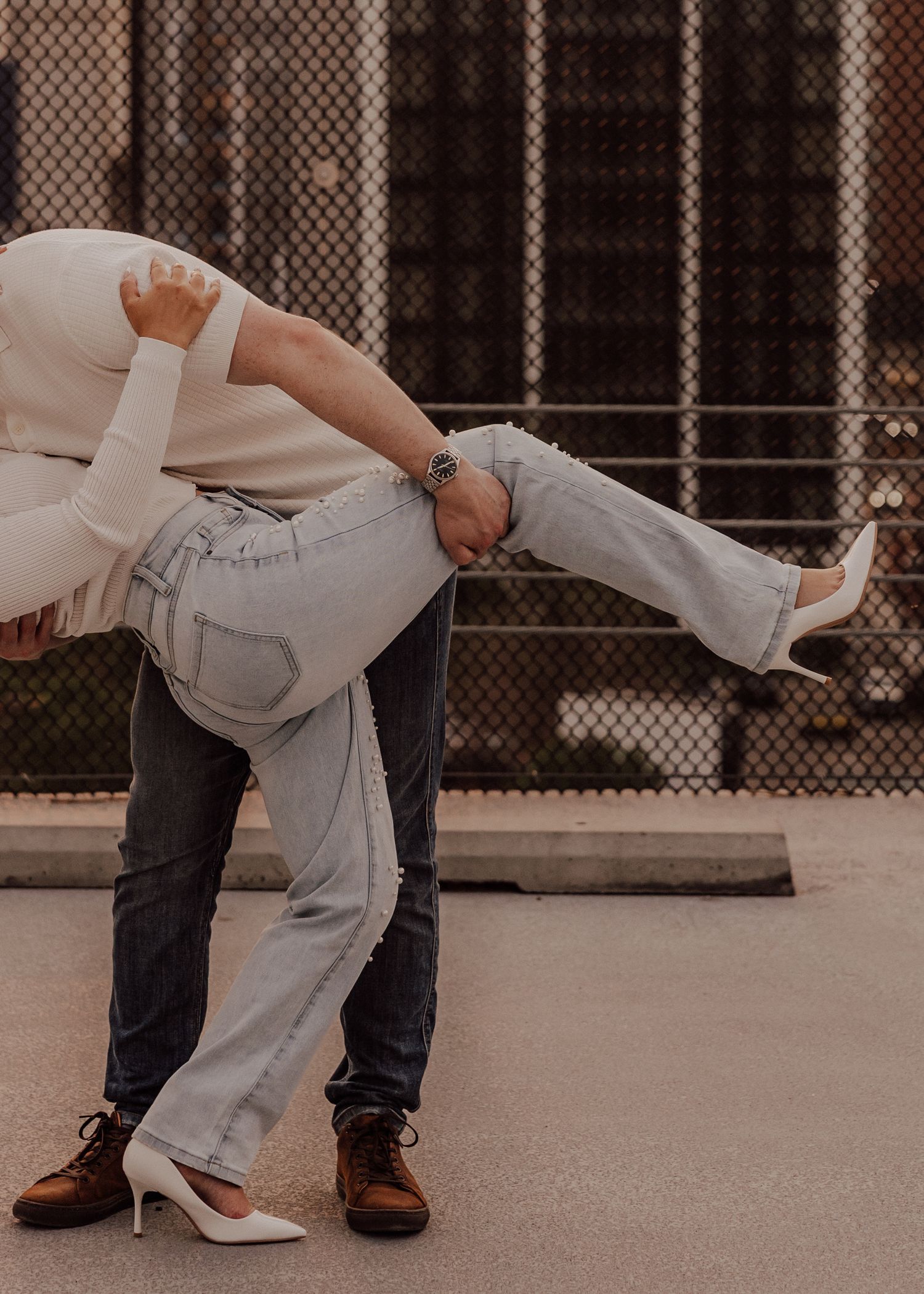 Romantic dip pose against urban rooftop setting with chain-link fence.