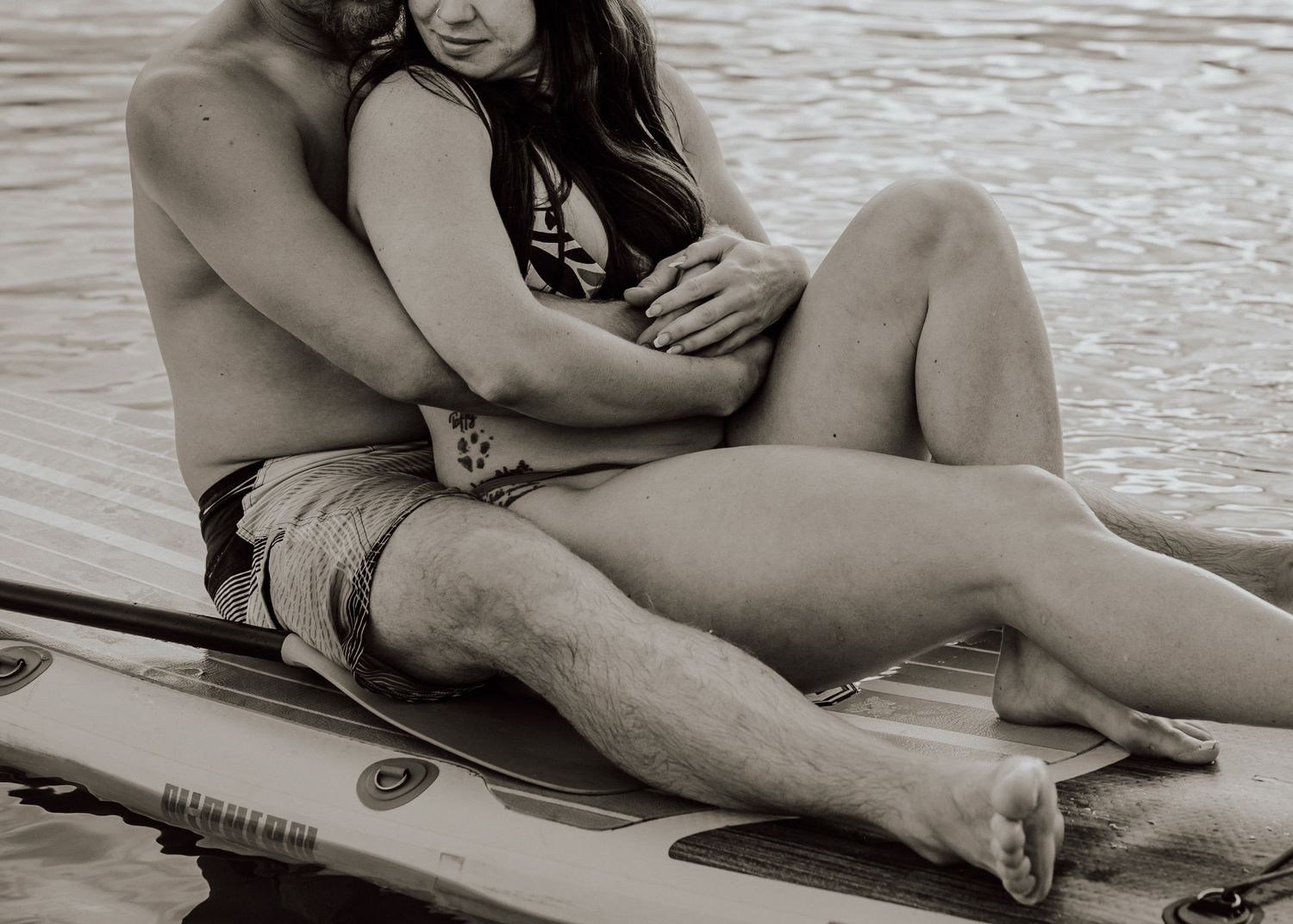Romantic couple sitting together on a paddleboard on calm water in a black and white photo.