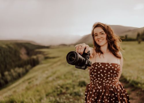 Photographer in polka dot dress captures images in golden mountain landscape.