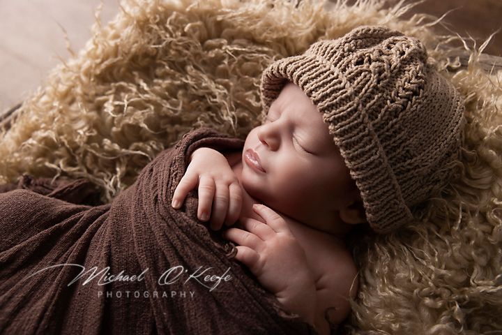 Peaceful newborn in knit hat resting on brown textured backdrop.