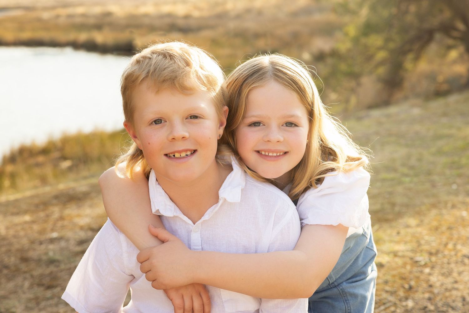 Siblings playing together outdoors in a golden autumn field at sunset.