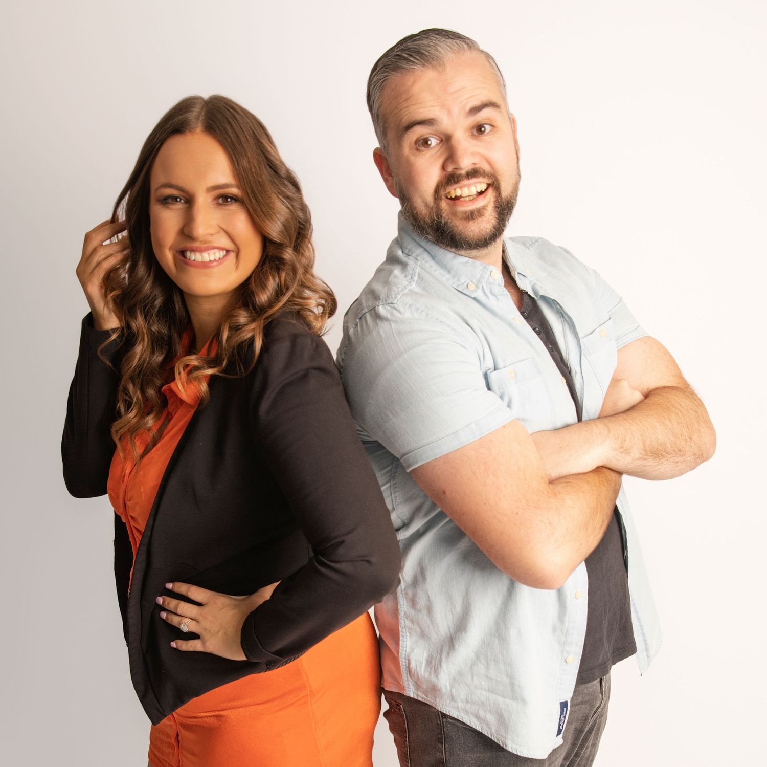 Two people in contrasting outfits pose back-to-back in studio setting.