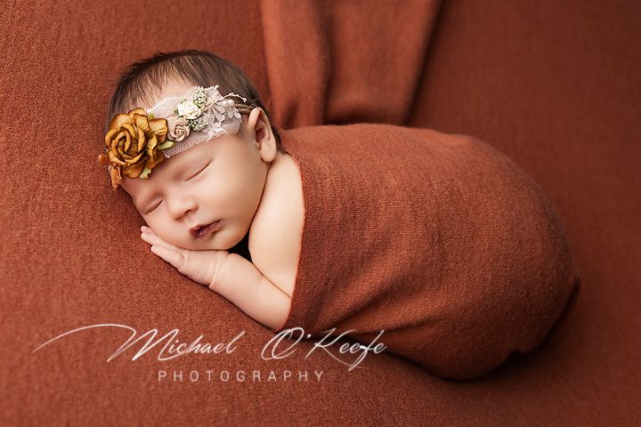 A sleeping newborn baby wrapped in brown fabric during a professional photography session.