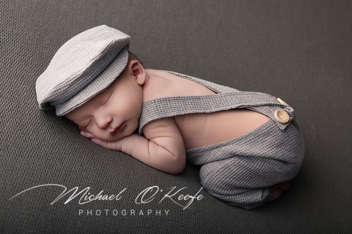 A series of black and white newborn photography portraits showing a sleeping baby in soft grey wraps and caps.