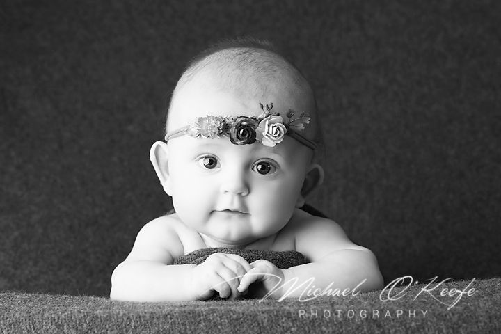 Black and white portrait series showing a baby's different expressions and poses on a dark background.