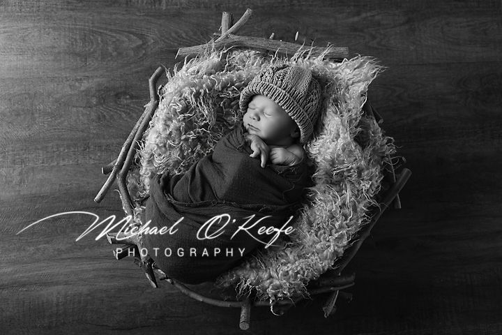 Black and white artistic photo showing a sleeping newborn nestled in soft textured blankets and delicate feathers.