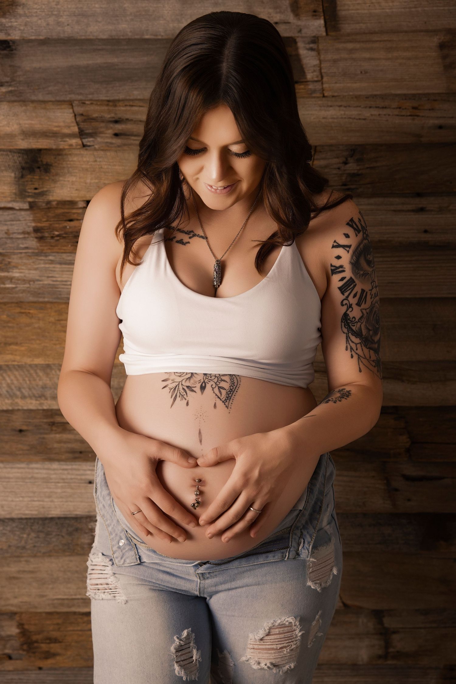 A series of maternity photos showing a pregnant person in ripped jeans and white tank top against a rustic wood wall.
