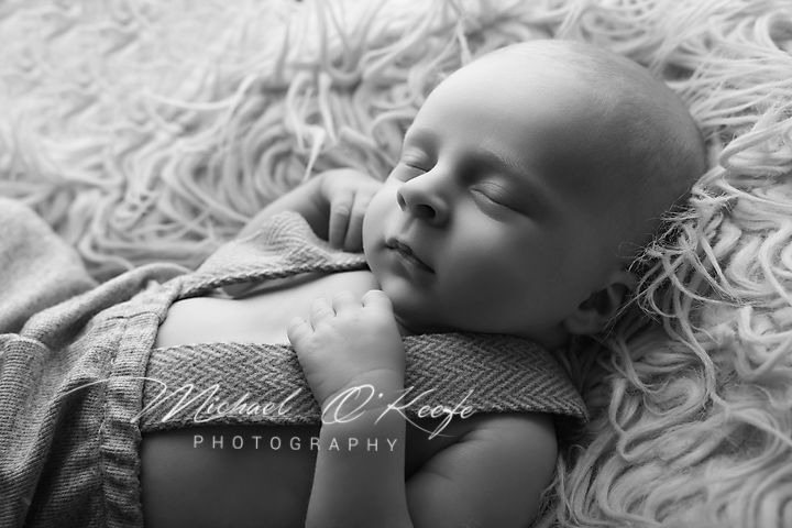 Black and white newborn photography of a sleeping baby wrapped in a knit blanket on a fluffy rug.