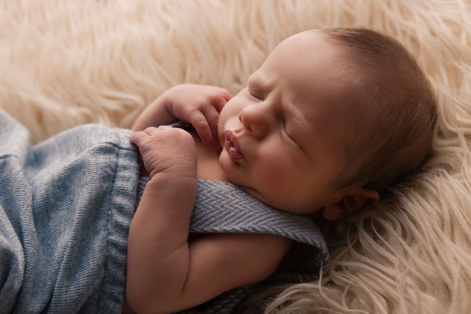 Newborn baby sleeping peacefully on soft white fur blanket in natural light.