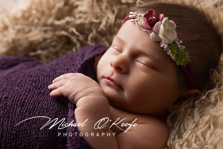 Newborn baby sleeping peacefully on soft cream-colored blanket with delicate floral headband.