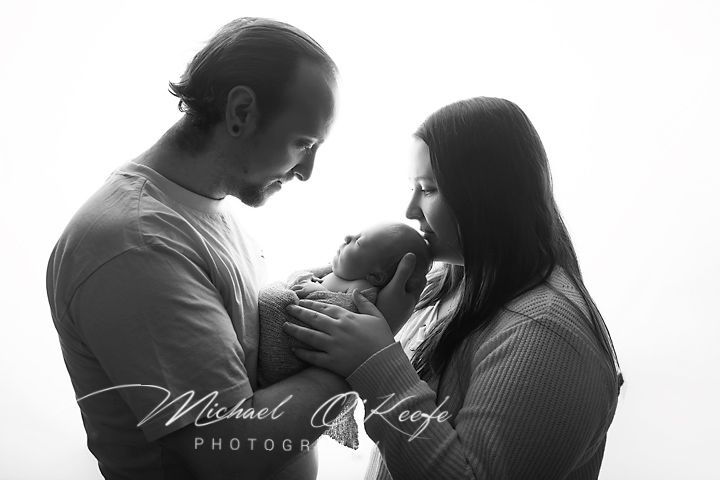 Black and white newborn family portrait of parents lovingly gazing at their sleeping baby, by Michael O'Keefe Photography.