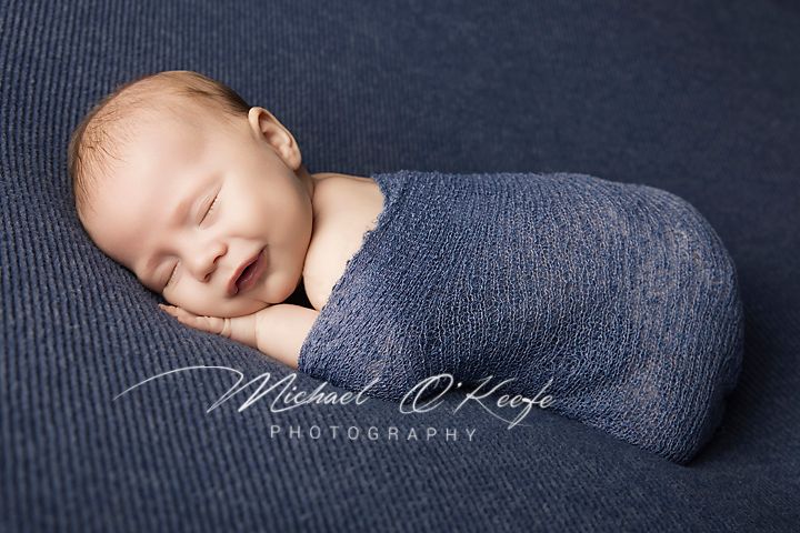 Sleeping newborn baby wrapped in blue knit fabric, Michael O'Keefe Photography.