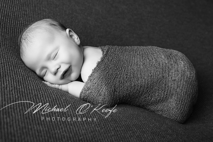 Black and white newborn photo of a sleeping baby swaddled in a knit wrap by Michael O'Keefe Photography.