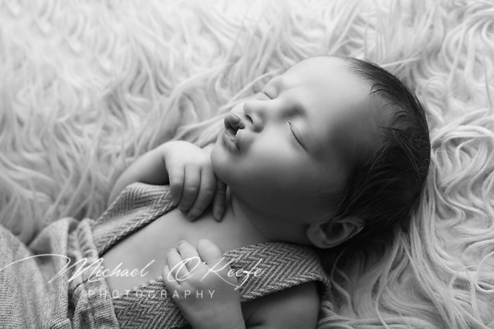 A sleeping baby lies on soft white blankets in black and white artistic photography.