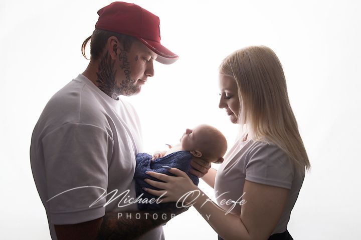 Parents lovingly gazing at their newborn baby in a bright studio portrait by Michael O'Keefe Photography.