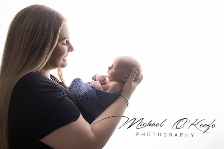A mother tenderly holds her newborn baby in a professional portrait by Michael O'Keefe Photography.