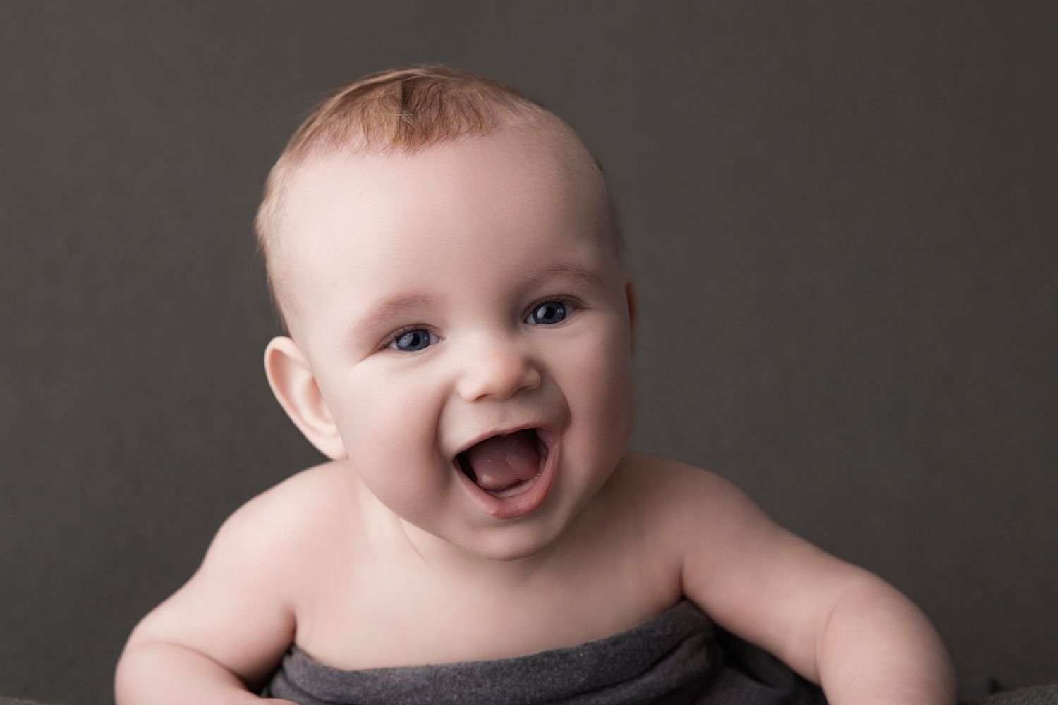 Happy baby showing pure joy with big smile on dark background.