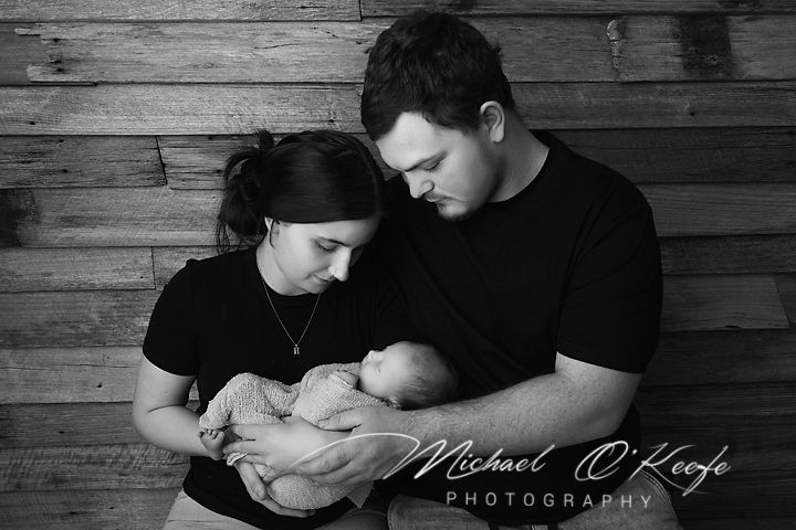 Black and white newborn photo of parents tenderly cradling their sleeping baby, by Michael O'Keefe Photography.