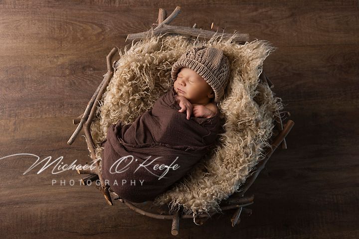 Newborn baby sleeps peacefully in rustic wooden crate lined with soft straw on dark wooden floor.