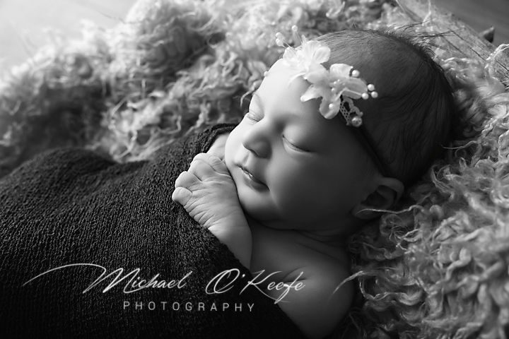 Black and white newborn portrait of sleeping baby girl with floral headband by Michael O'Keefe Photography.