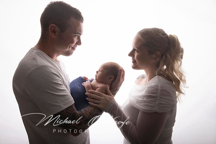 A couple gazes lovingly at their newborn baby wrapped in blue during a professional newborn photography session.