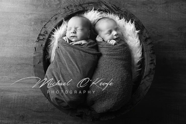 Black and white photo of an infant sleeping peacefully in soft blankets while curled up in fetal position.