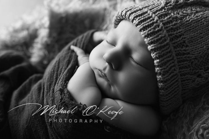 Black and white newborn photography of a sleeping baby wearing a knit hat, by Michael O'Keefe Photography.