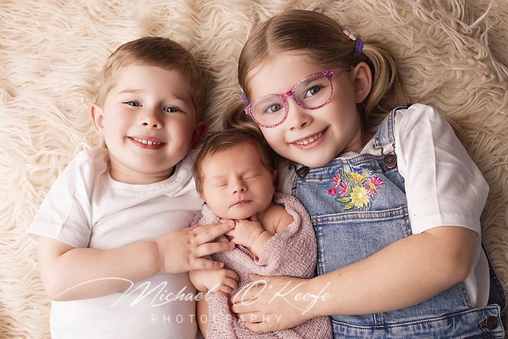 Children lying together on a white bed with soft pillows and blankets in a series of sweet sibling poses.