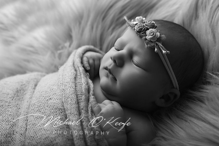 Black and white newborn photography of a sleeping baby wrapped in soft fabric wearing a floral headband.
