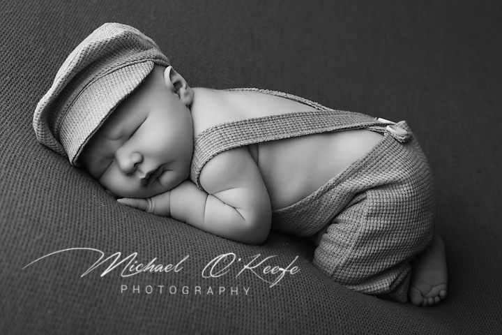 Sleeping newborn baby in black and white photo wearing suspenders and newsboy cap by Michael O'Keefe Photography.