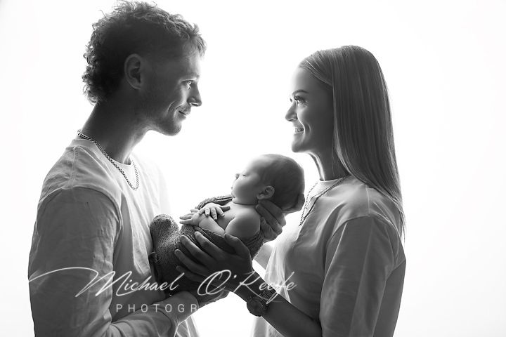 Black and white portrait of parents gazing lovingly at their newborn baby in a tender family moment.
