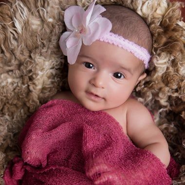 Sweet newborn photography series featuring baby in burgundy wrap surrounded by soft textures.