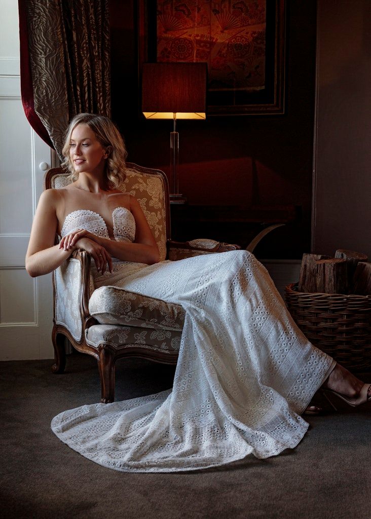Artistic bridal portraits in a dark moody interior showing a white lace dress against vintage furniture.