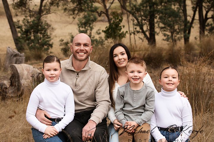 Candid family photo session in casual attire among tall trees and natural scenery.