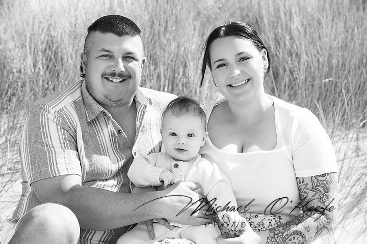 Family wearing white clothes lies in tall grass field during outdoor photo session.