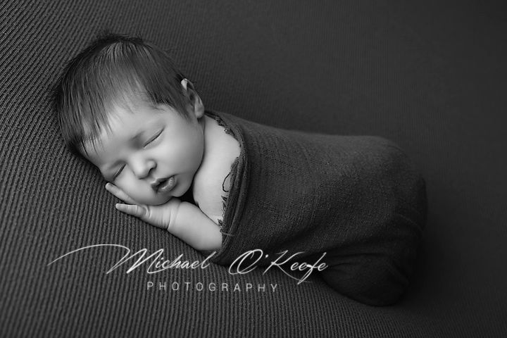 Black and white newborn photography of a sleeping baby swaddled in a soft wrap by Michael O'Keefe Photography.
