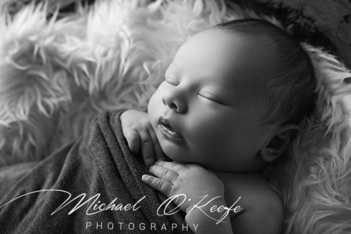 Black and white newborn photography by Michael O'Keefe capturing a peacefully sleeping baby wrapped in a soft blanket.