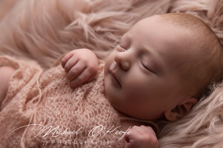 Sleeping newborn baby in pink knit wrap on textured background.