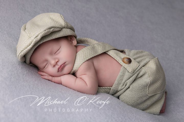 Sleeping infant in vintage newsboy cap and overalls captured in artistic portrait.