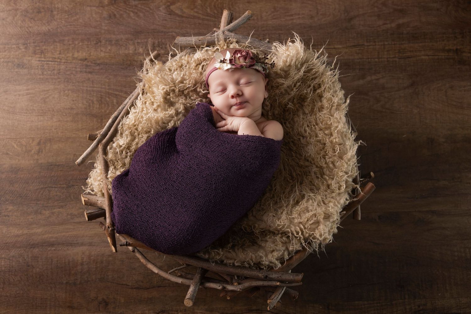 Sleeping newborn wrapped in purple blanket nestled in rustic nest setting.