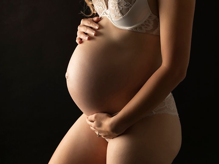 Silhouette of pregnant woman's belly in lingerie against dark background.