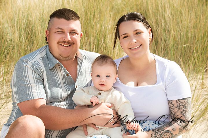 Family sits together in golden field during sunset photo session.
