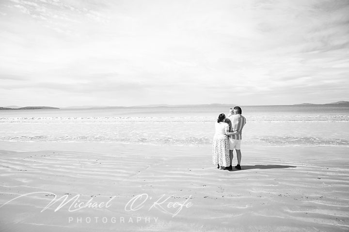 A black and white panoramic sequence of a couple sitting together on a beach at sunset.