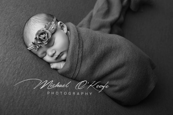 Black and white newborn portrait of a swaddled baby with floral headband, by Michael O'Keefe Photography.