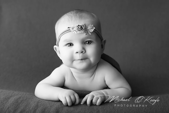 Black and white portrait of a cute baby girl wearing a floral headband, lying on a soft blanket.