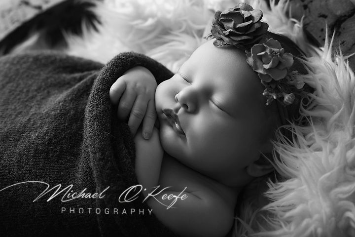 Black and white newborn photo of sleeping baby with floral headband wrapped in soft blanket by Michael O'Keefe Photography.