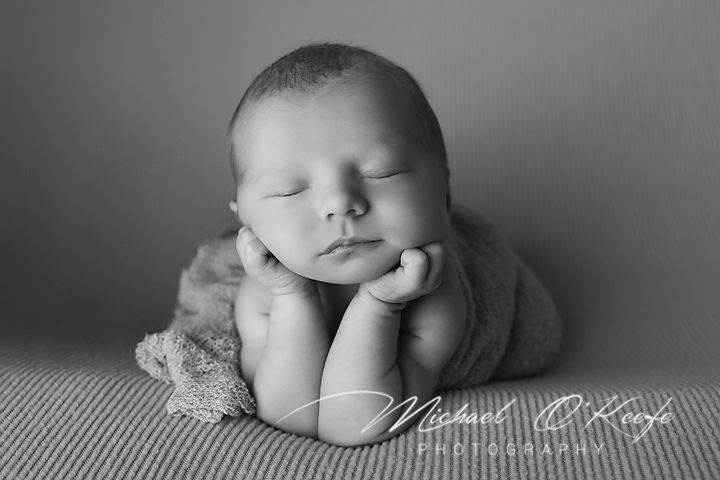 Sleeping newborn baby wrapped in soft gray blanket in black and white portrait photography.