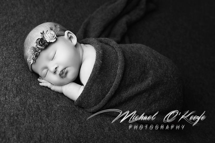 Black and white portrait of sleeping newborn in dark wrap with floral crown.